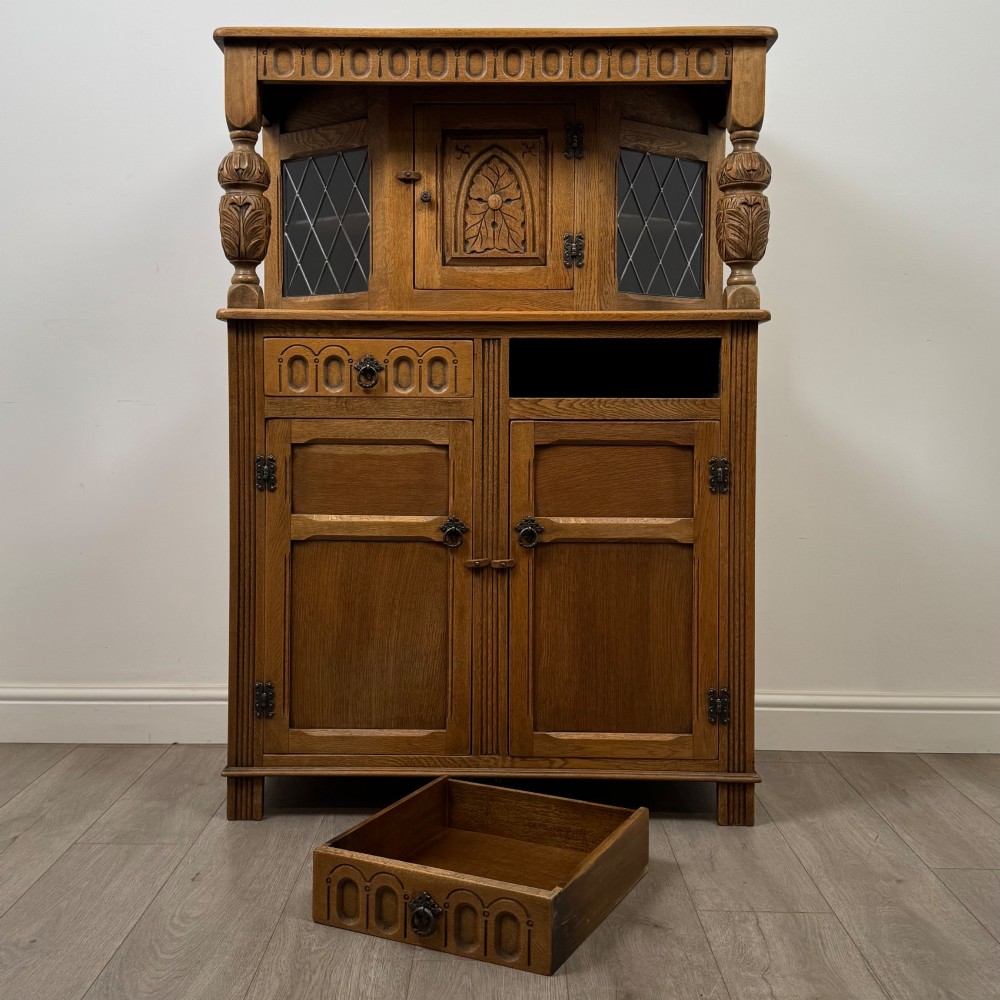 A twentieth-century golden oak court cupboard featuring carved panels, leaded glass side doors, and turned bulbous supports. View XI