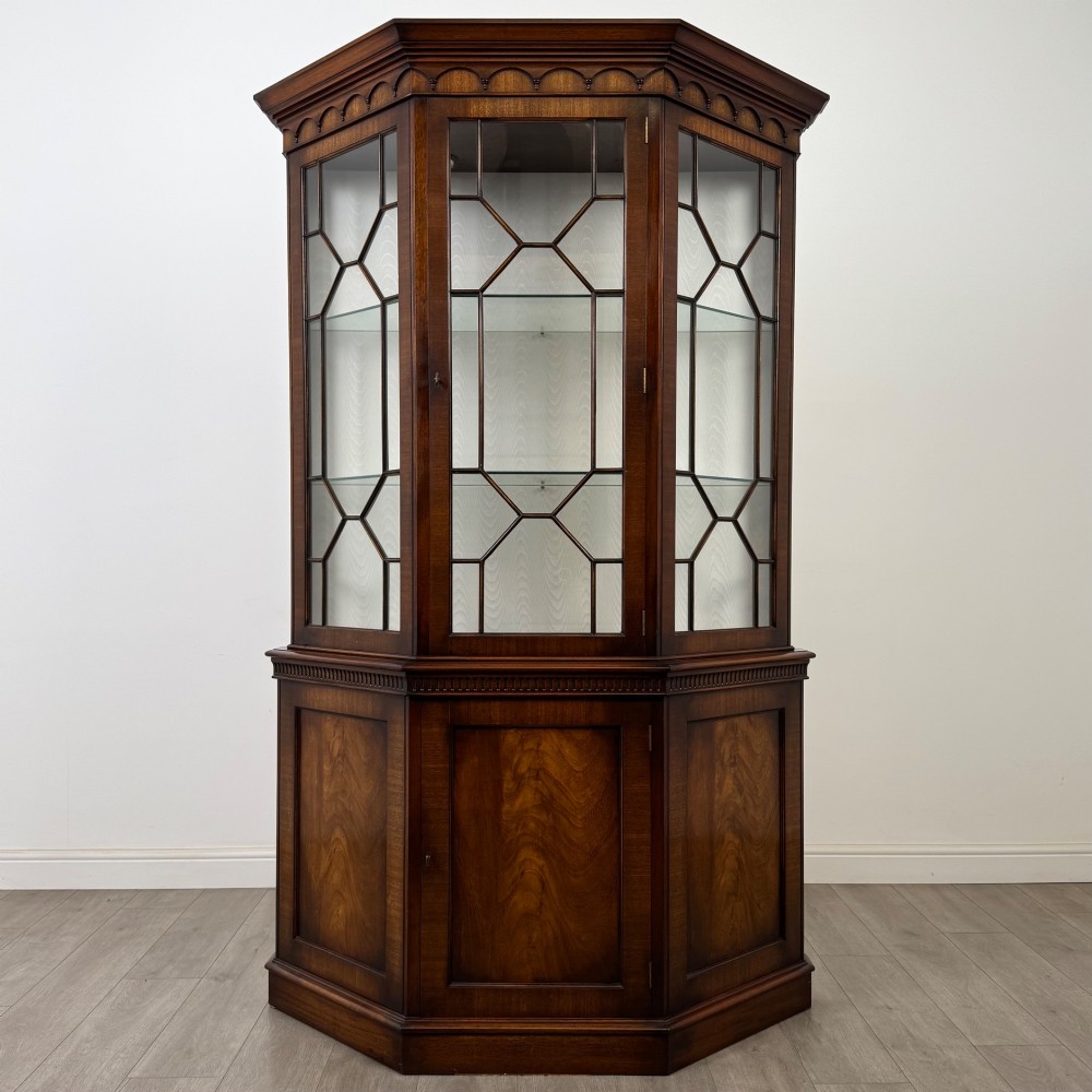 A tall mahogany display cabinet featuring astragal glazed upper doors, glass shelving, and flame mahogany lower panel doors with a canted front.