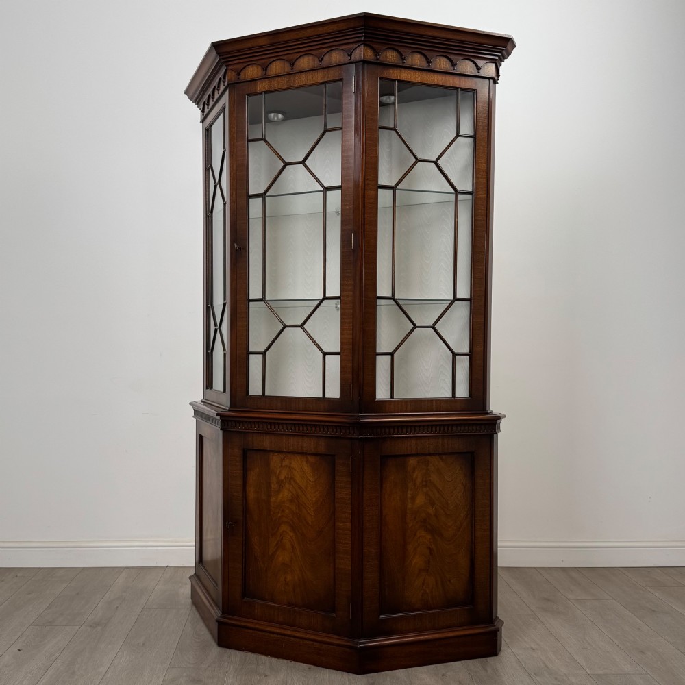 A tall mahogany display cabinet featuring astragal glazed upper doors, glass shelving, and flame mahogany lower panel doors with a canted front. View III
