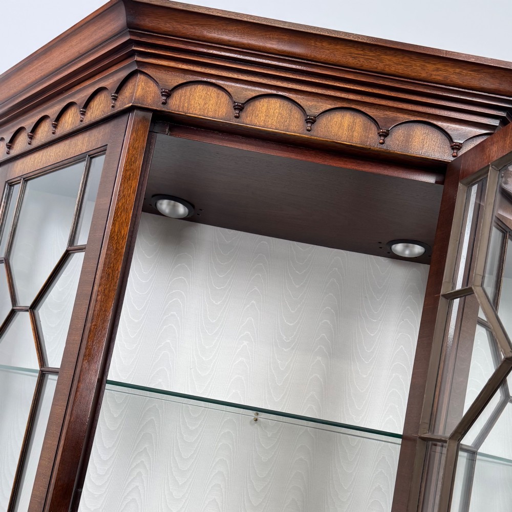 A tall mahogany display cabinet featuring astragal glazed upper doors, glass shelving, and flame mahogany lower panel doors with a canted front. View X