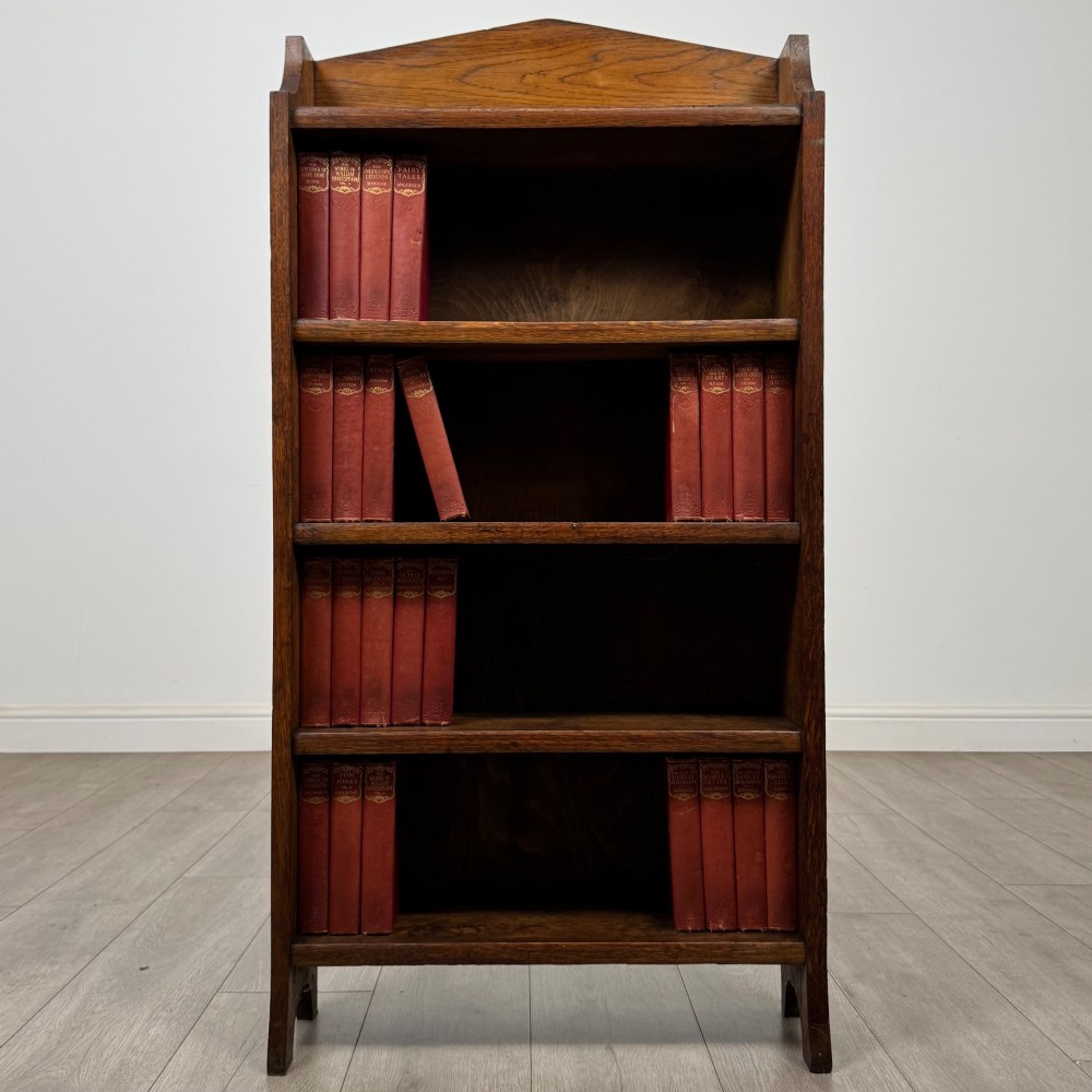 A freestanding Edwardian open oak bookcase featuring four tiers of shelves and a gabled top gallery.