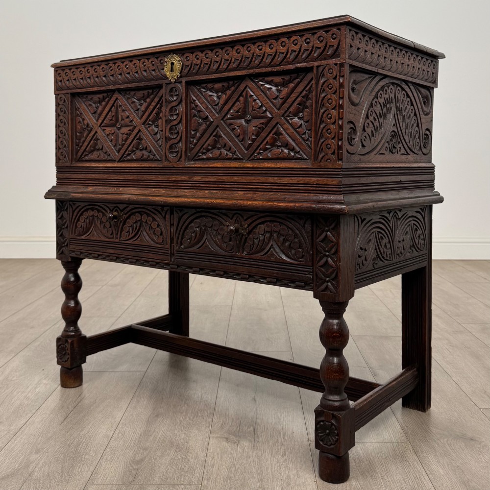 A 19th-century carved dark oak chest on stand featuring geometric relief panels, brass keyhole escutcheon, lower drawers, and turned legs. View II