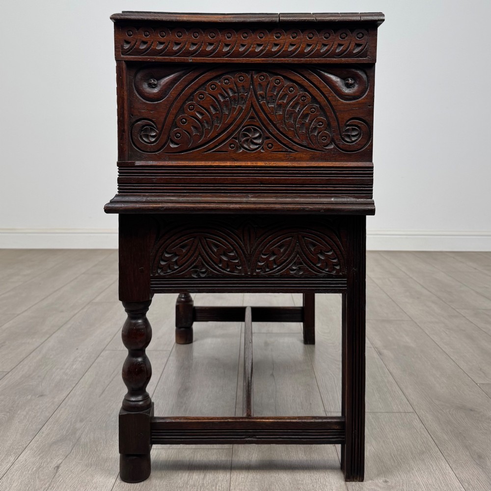 A 19th-century carved dark oak chest on stand featuring geometric relief panels, brass keyhole escutcheon, lower drawers, and turned legs. View III