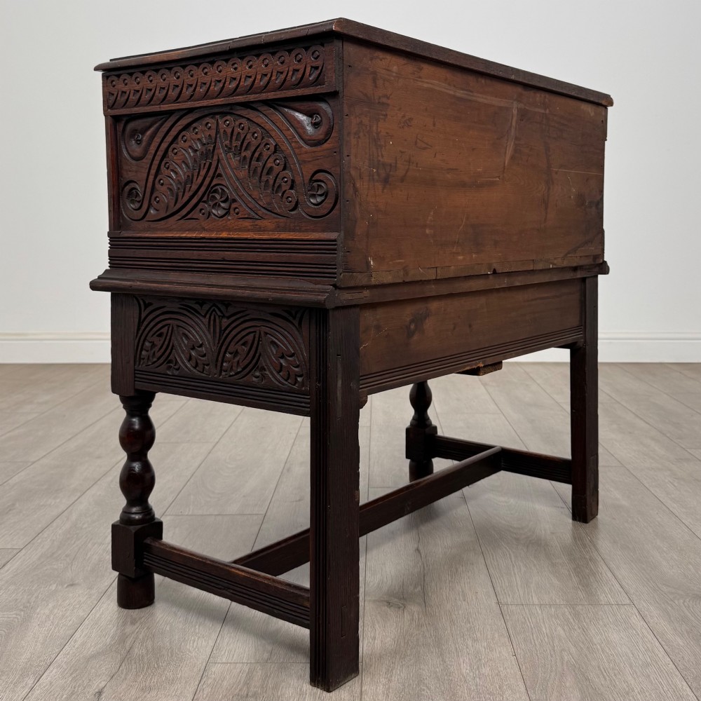 A 19th-century carved dark oak chest on stand featuring geometric relief panels, brass keyhole escutcheon, lower drawers, and turned legs. View IV