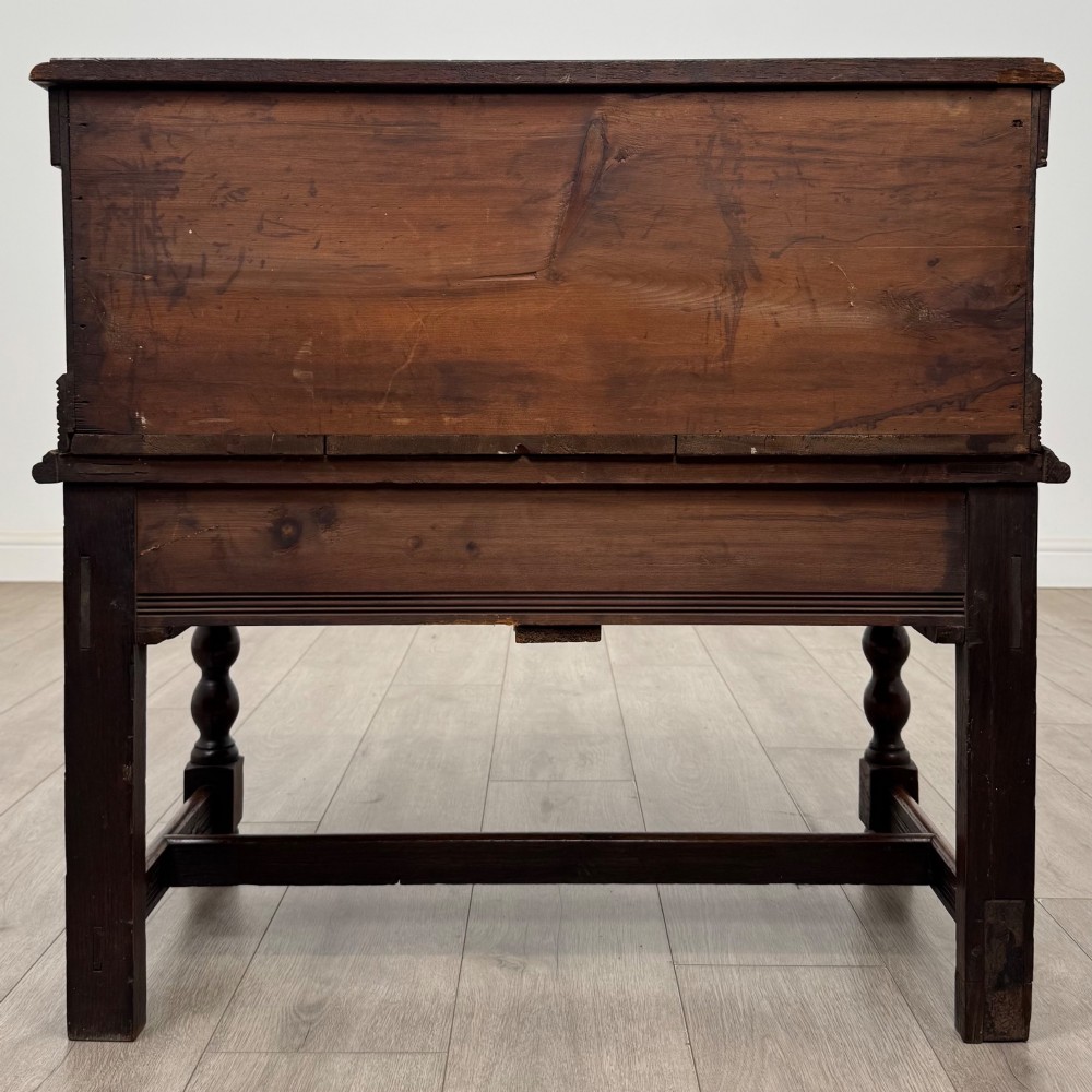 A 19th-century carved dark oak chest on stand featuring geometric relief panels, brass keyhole escutcheon, lower drawers, and turned legs. View V