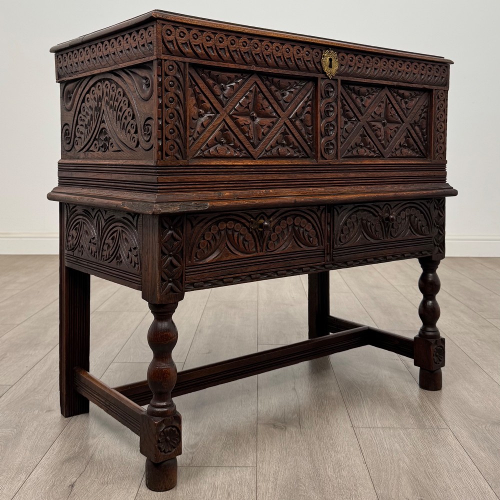 A 19th-century carved dark oak chest on stand featuring geometric relief panels, brass keyhole escutcheon, lower drawers, and turned legs. View VIII