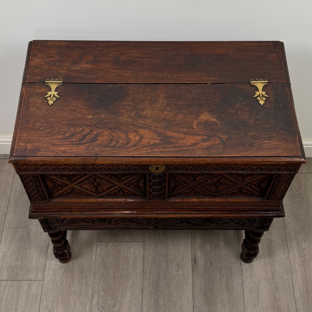 A 19th-century carved dark oak chest on stand featuring geometric relief panels, brass keyhole escutcheon, lower drawers, and turned legs. View IX
