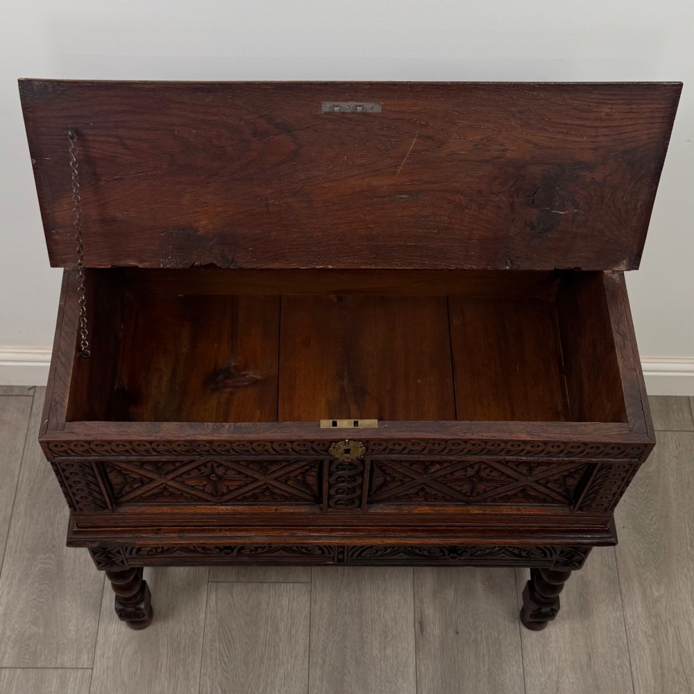 A 19th-century carved dark oak chest on stand featuring geometric relief panels, brass keyhole escutcheon, lower drawers, and turned legs. View X