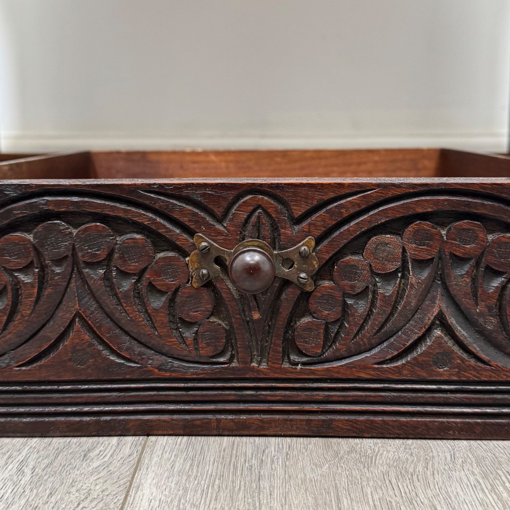 A 19th-century carved dark oak chest on stand featuring geometric relief panels, brass keyhole escutcheon, lower drawers, and turned legs. View XII