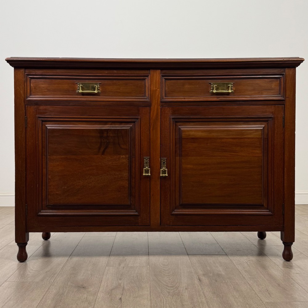 An antique Edwardian mahogany sideboard featuring two top drawers with brass drop handles above two field-panelled cupboard doors, resting on short turned feet.