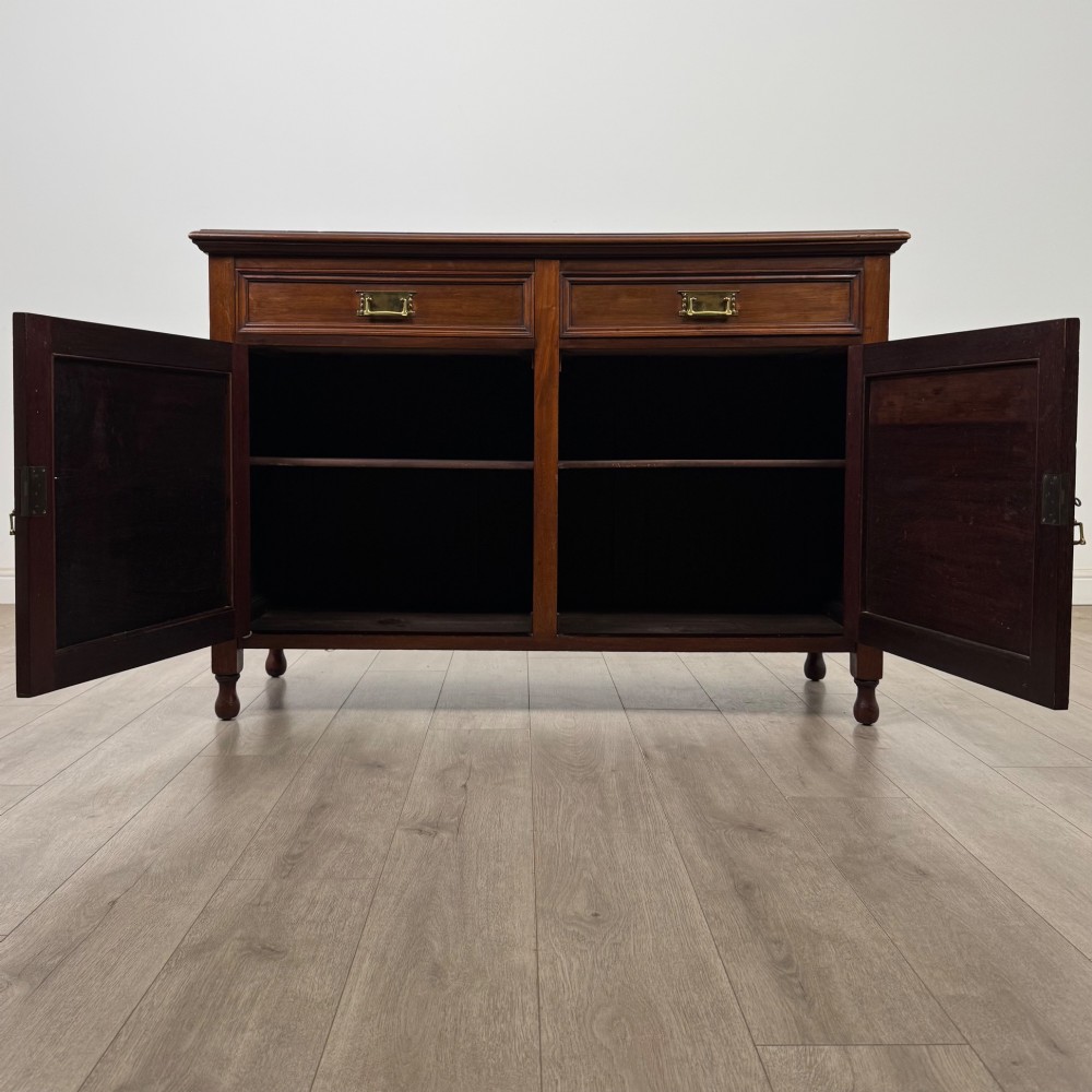 An antique Edwardian mahogany sideboard featuring two top drawers with brass drop handles above two field-panelled cupboard doors, resting on short turned feet. View II