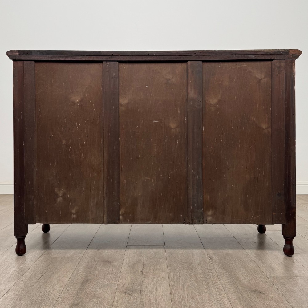An antique Edwardian mahogany sideboard featuring two top drawers with brass drop handles above two field-panelled cupboard doors, resting on short turned feet. View VI