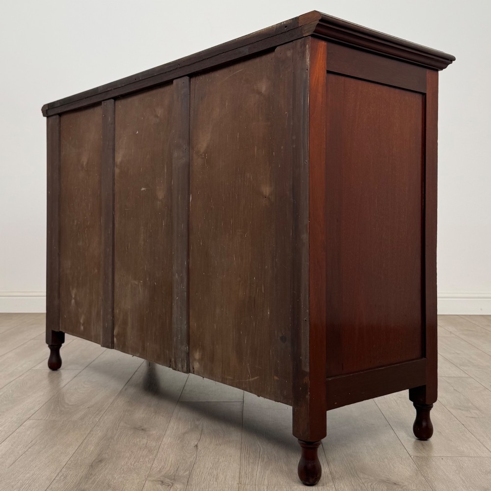 An antique Edwardian mahogany sideboard featuring two top drawers with brass drop handles above two field-panelled cupboard doors, resting on short turned feet. View VII