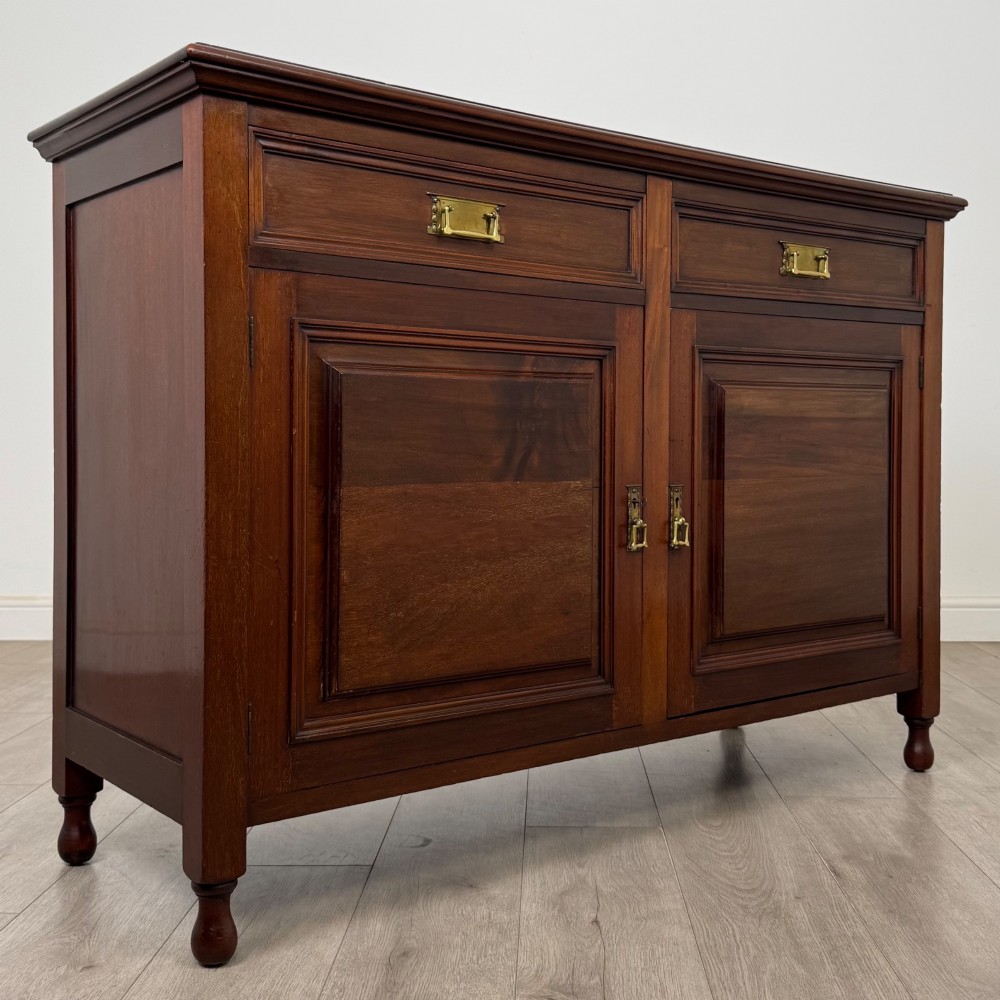 An antique Edwardian mahogany sideboard featuring two top drawers with brass drop handles above two field-panelled cupboard doors, resting on short turned feet. View IX