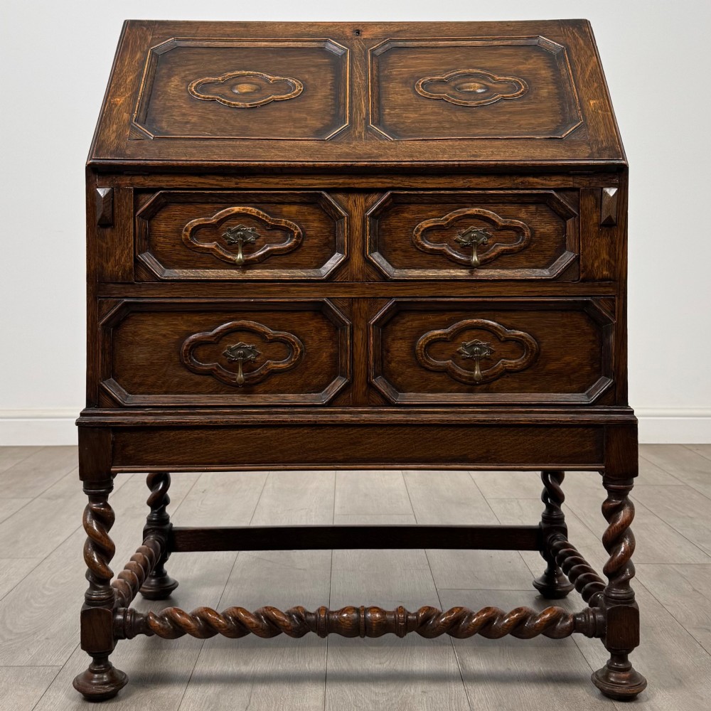 A dark oak Jacobean revival slant-front bureau featuring geometric panel mouldings, drop handles, and barley twist legs joined by stretchers.