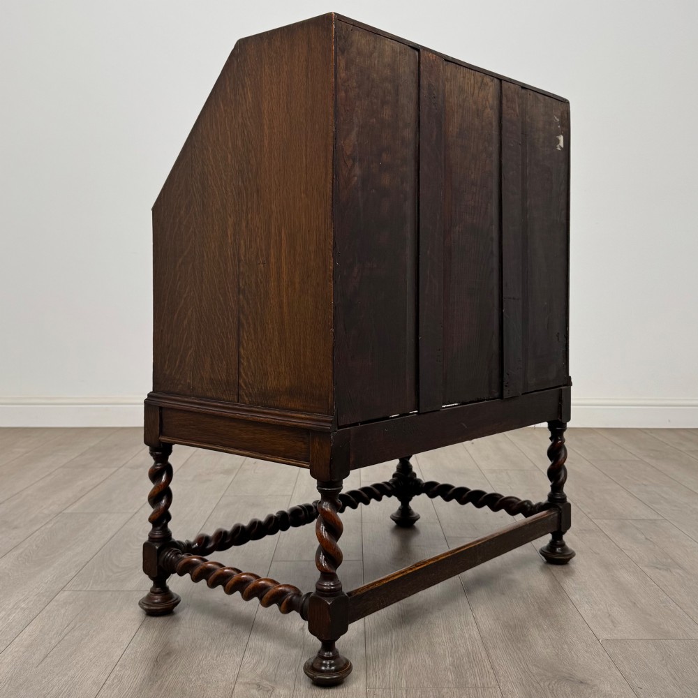 A dark oak Jacobean revival slant-front bureau featuring geometric panel mouldings, drop handles, and barley twist legs joined by stretchers. View V
