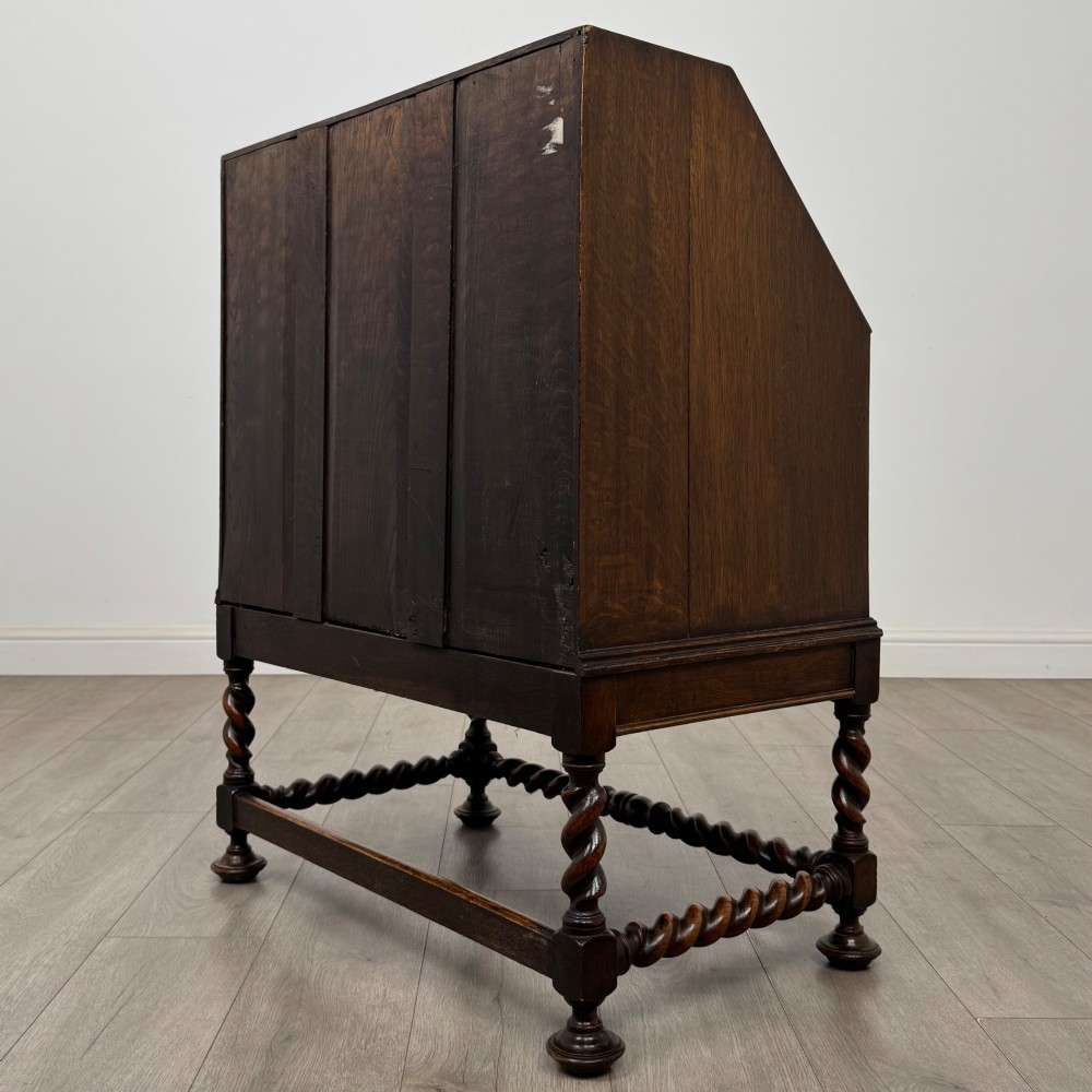 A dark oak Jacobean revival slant-front bureau featuring geometric panel mouldings, drop handles, and barley twist legs joined by stretchers. View VII