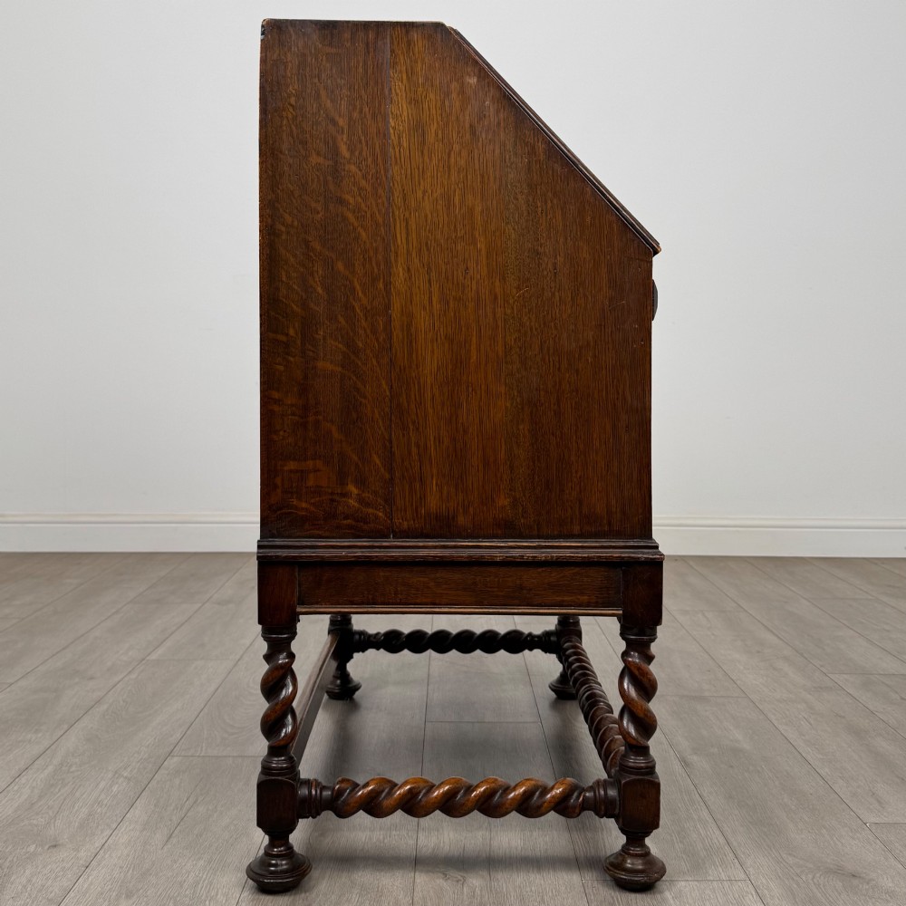 A dark oak Jacobean revival slant-front bureau featuring geometric panel mouldings, drop handles, and barley twist legs joined by stretchers. View VIII