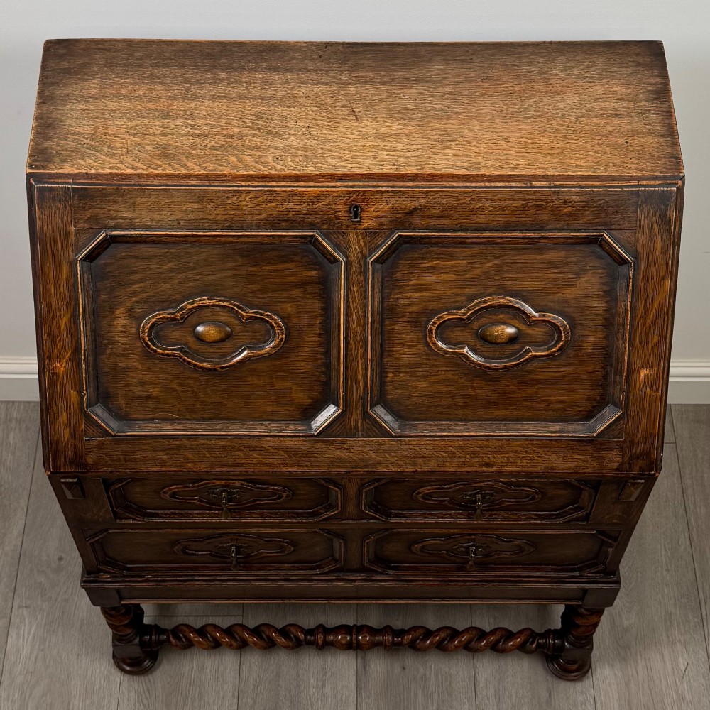 A dark oak Jacobean revival slant-front bureau featuring geometric panel mouldings, drop handles, and barley twist legs joined by stretchers. View X