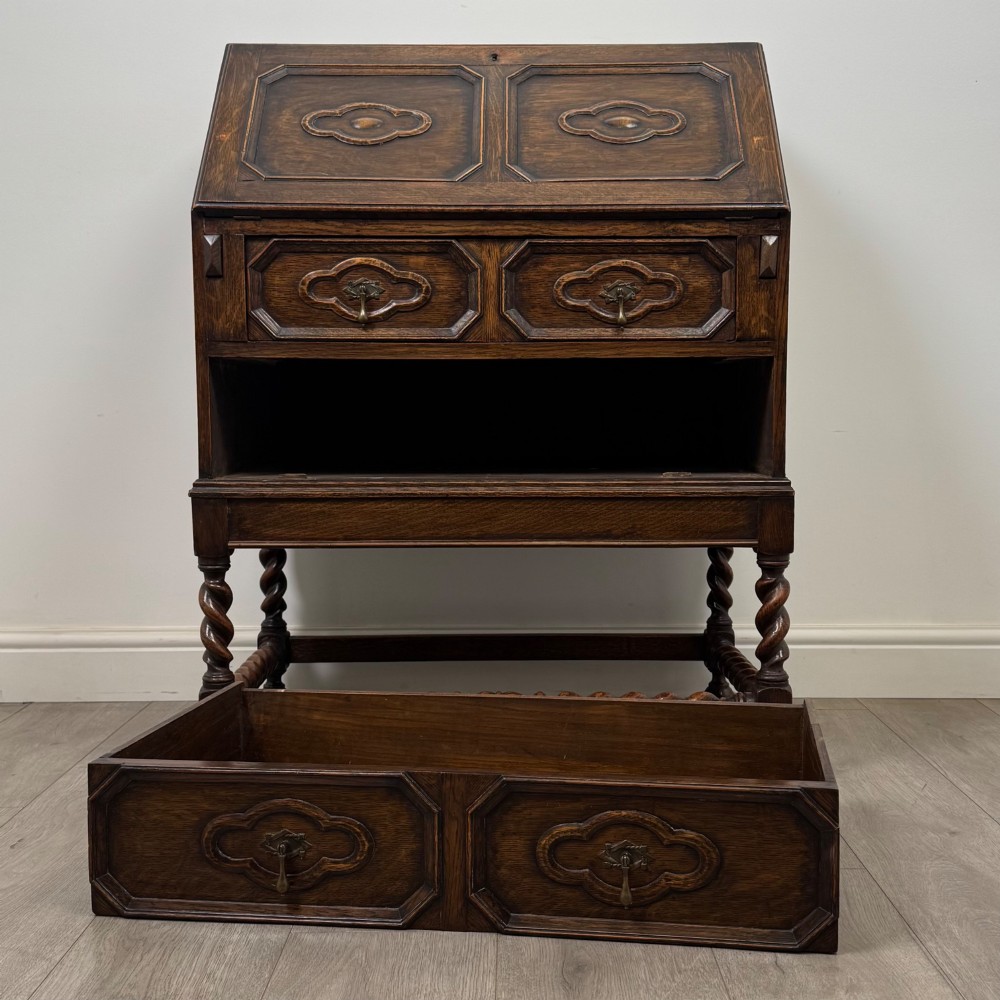 A dark oak Jacobean revival slant-front bureau featuring geometric panel mouldings, drop handles, and barley twist legs joined by stretchers. View XII