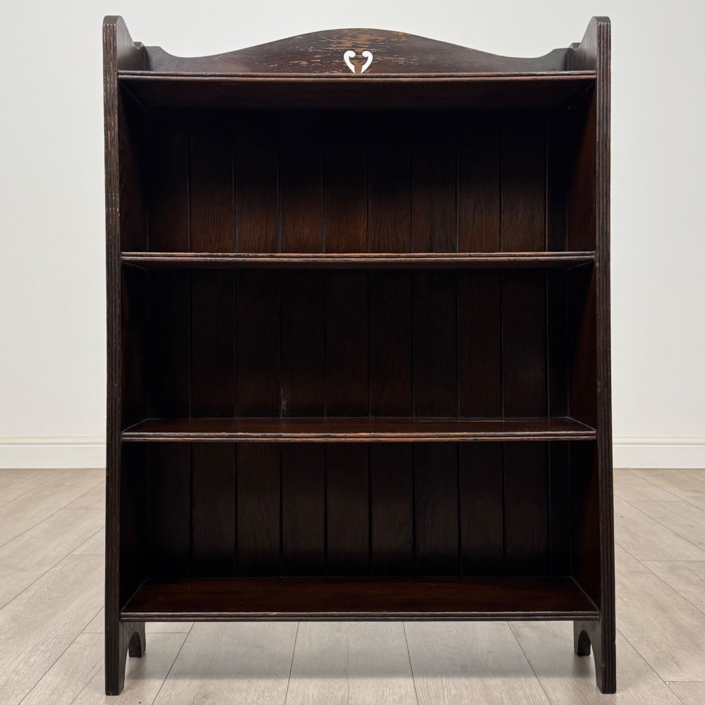 A dark brown oak open bookcase featuring three tiers, vertical plank backboard, and a shaped top rail with a central cut-out motif. View II