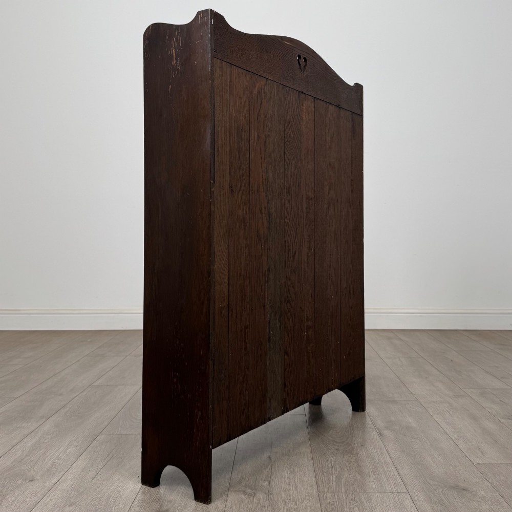 A dark brown oak open bookcase featuring three tiers, vertical plank backboard, and a shaped top rail with a central cut-out motif. View V