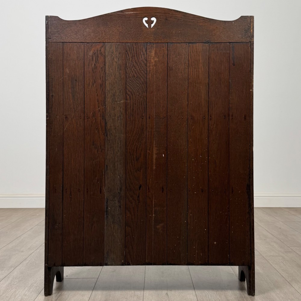 A dark brown oak open bookcase featuring three tiers, vertical plank backboard, and a shaped top rail with a central cut-out motif. View VI