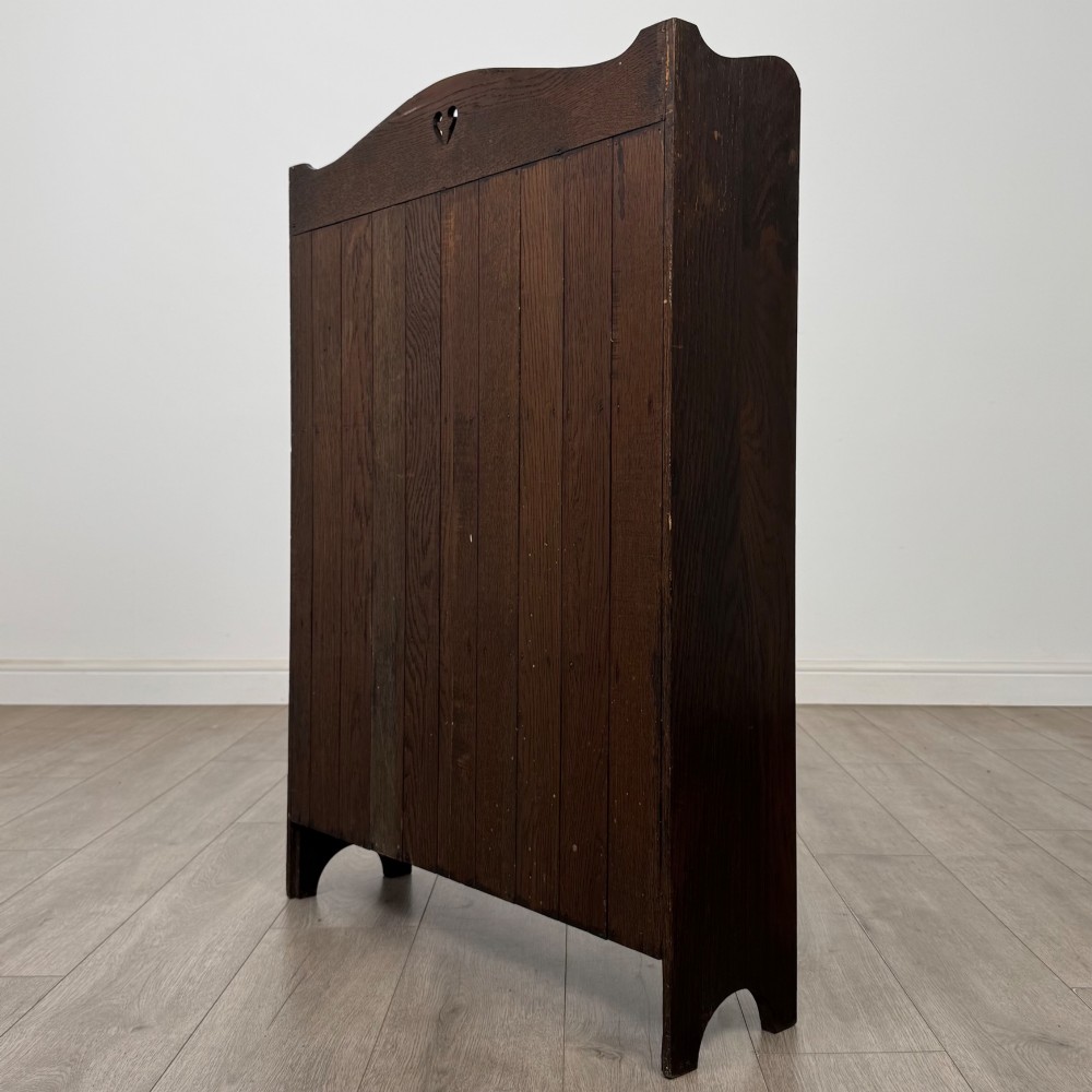 A dark brown oak open bookcase featuring three tiers, vertical plank backboard, and a shaped top rail with a central cut-out motif. View VII