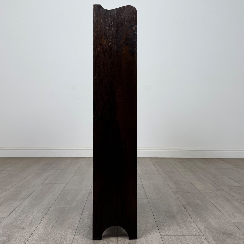 A dark brown oak open bookcase featuring three tiers, vertical plank backboard, and a shaped top rail with a central cut-out motif. View VIII