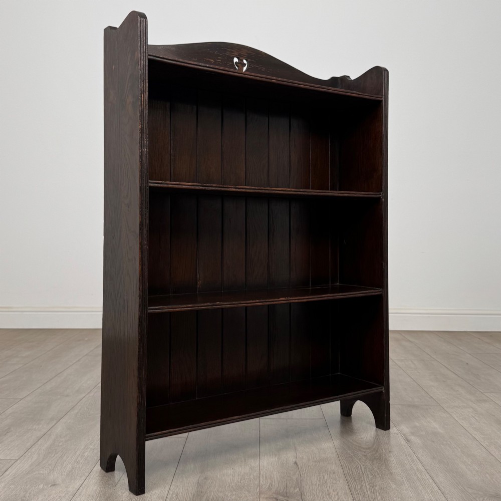 A dark brown oak open bookcase featuring three tiers, vertical plank backboard, and a shaped top rail with a central cut-out motif. View IX