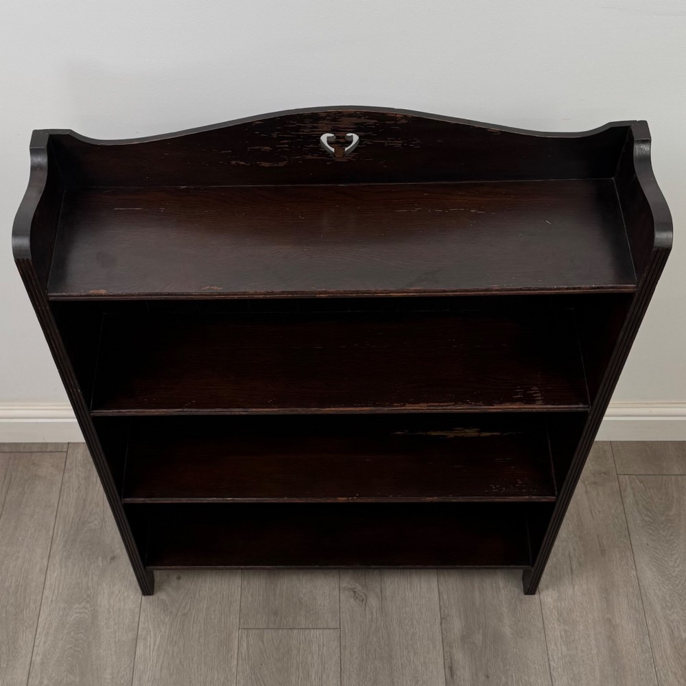 A dark brown oak open bookcase featuring three tiers, vertical plank backboard, and a shaped top rail with a central cut-out motif. View X