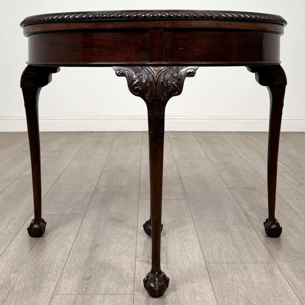 A circular dark mahogany card table featuring acanthus carved knees and cabriole legs terminating in ball and claw feet.