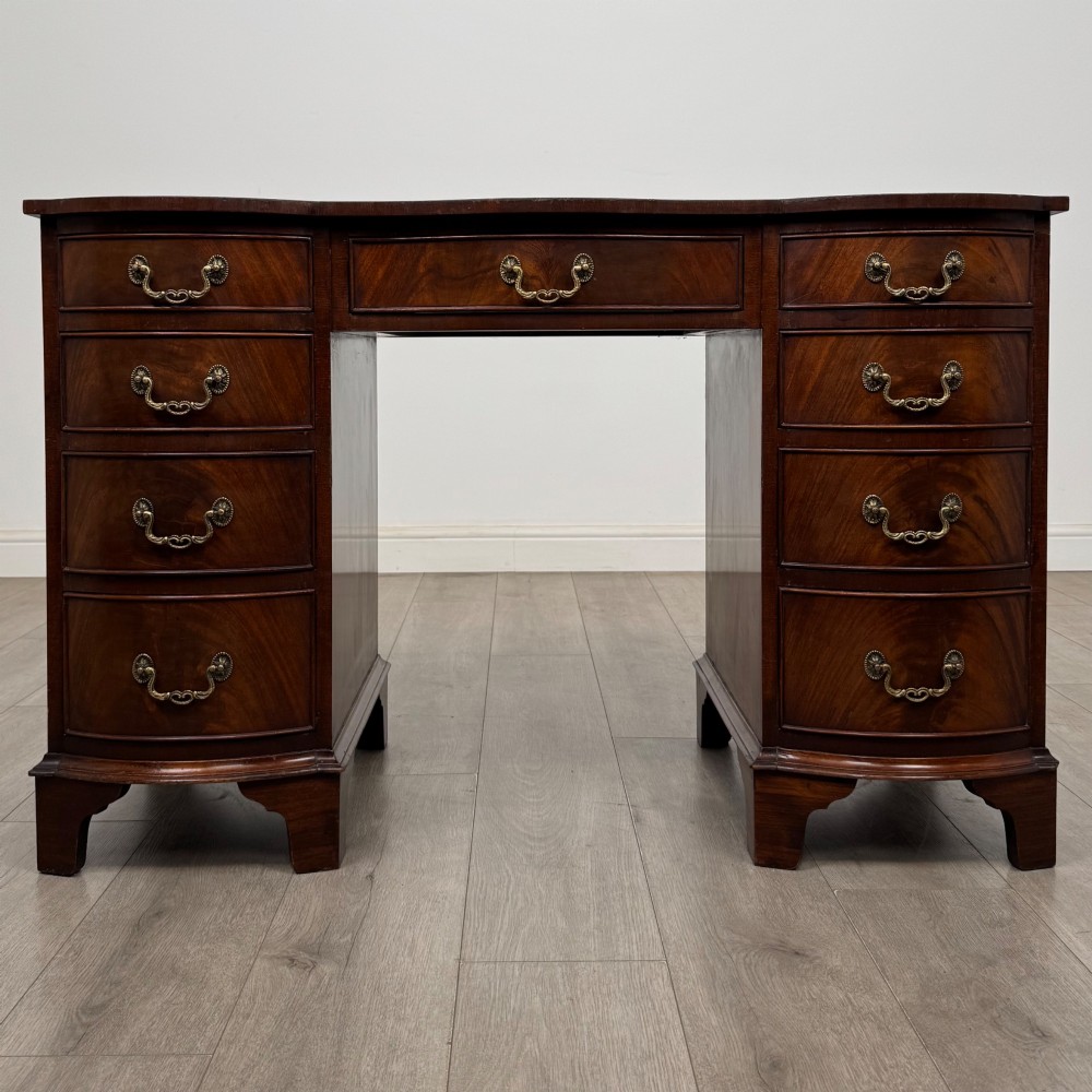 A twentieth-century mahogany kneehole desk featuring a serpentine front, multiple drawers with brass swan-neck handles, and bracket feet.