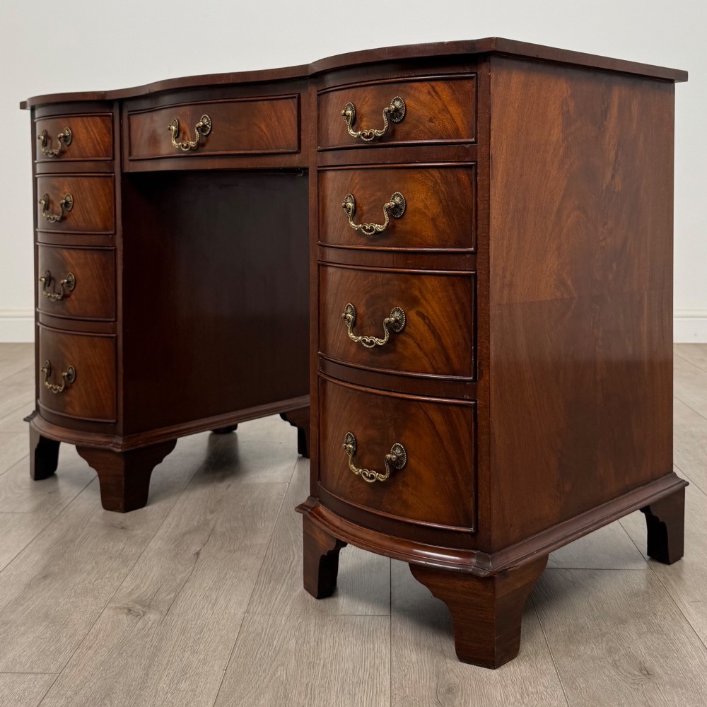 A twentieth-century mahogany kneehole desk featuring a serpentine front, multiple drawers with brass swan-neck handles, and bracket feet. View II