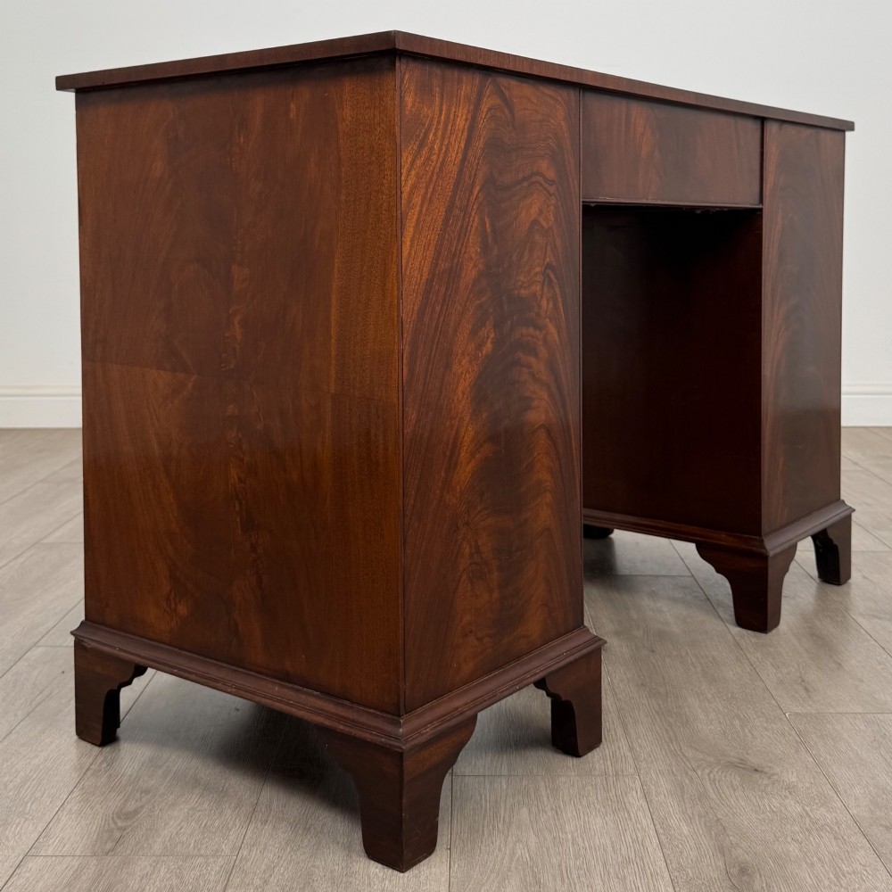 A twentieth-century mahogany kneehole desk featuring a serpentine front, multiple drawers with brass swan-neck handles, and bracket feet. View IV