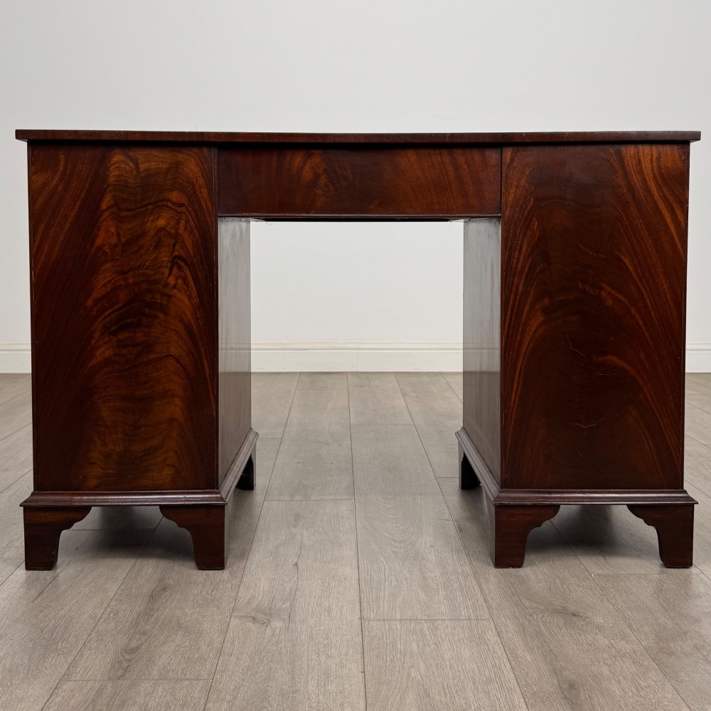 A twentieth-century mahogany kneehole desk featuring a serpentine front, multiple drawers with brass swan-neck handles, and bracket feet. View V