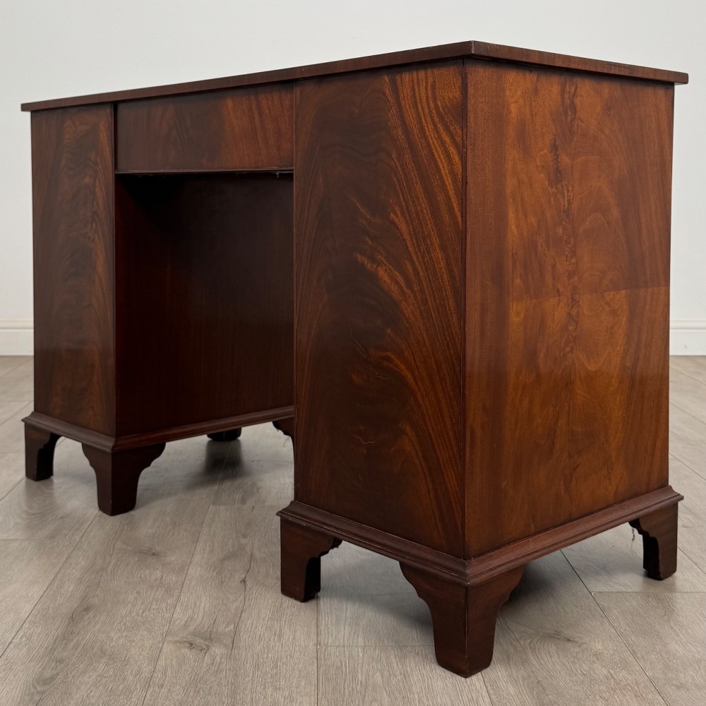 A twentieth-century mahogany kneehole desk featuring a serpentine front, multiple drawers with brass swan-neck handles, and bracket feet. View VI