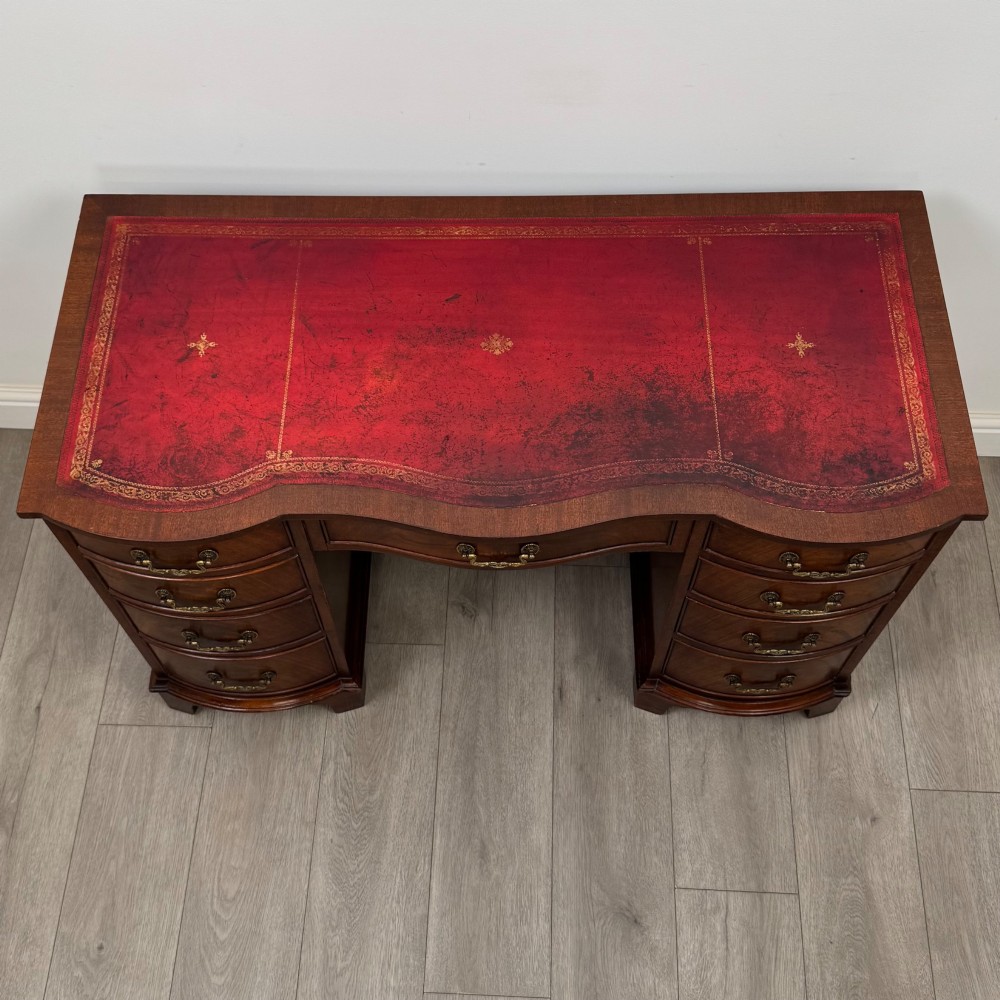 A twentieth-century mahogany kneehole desk featuring a serpentine front, multiple drawers with brass swan-neck handles, and bracket feet. View IX