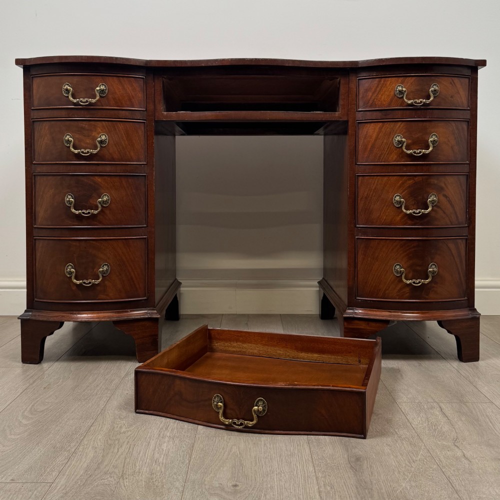 A twentieth-century mahogany kneehole desk featuring a serpentine front, multiple drawers with brass swan-neck handles, and bracket feet. View X