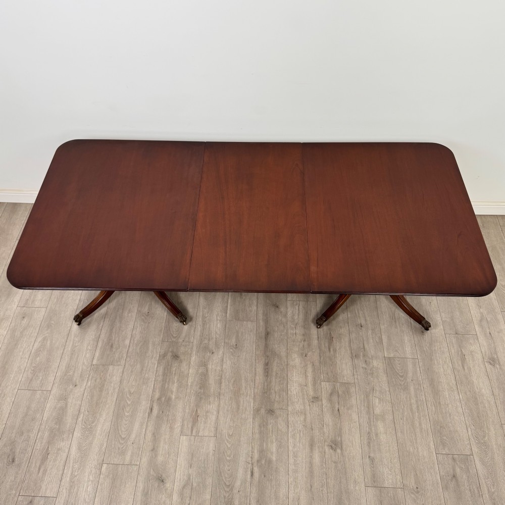 A 20th-century mahogany twin pedestal dining table featuring an extension leaf, reeded edges, and splayed quadruped feet with brass castors. View III