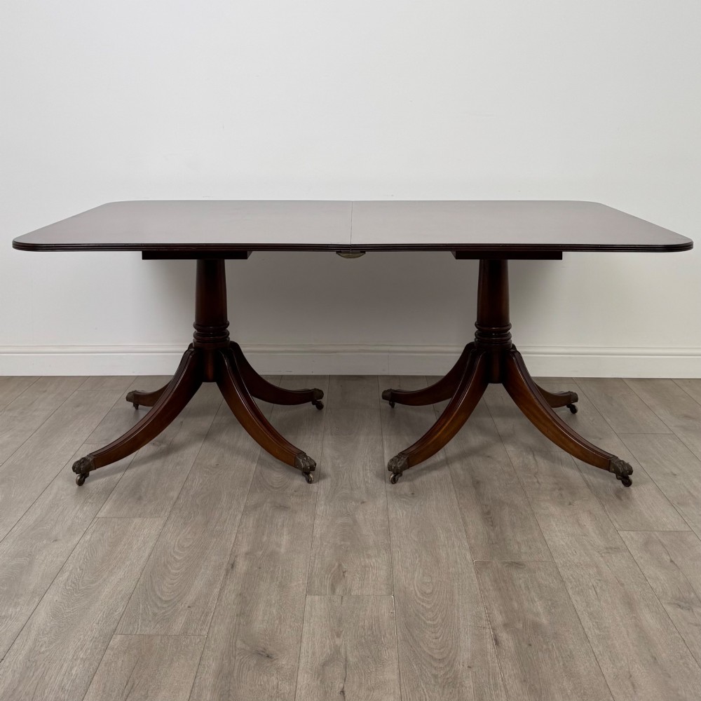 A 20th-century mahogany twin pedestal dining table featuring an extension leaf, reeded edges, and splayed quadruped feet with brass castors. View V