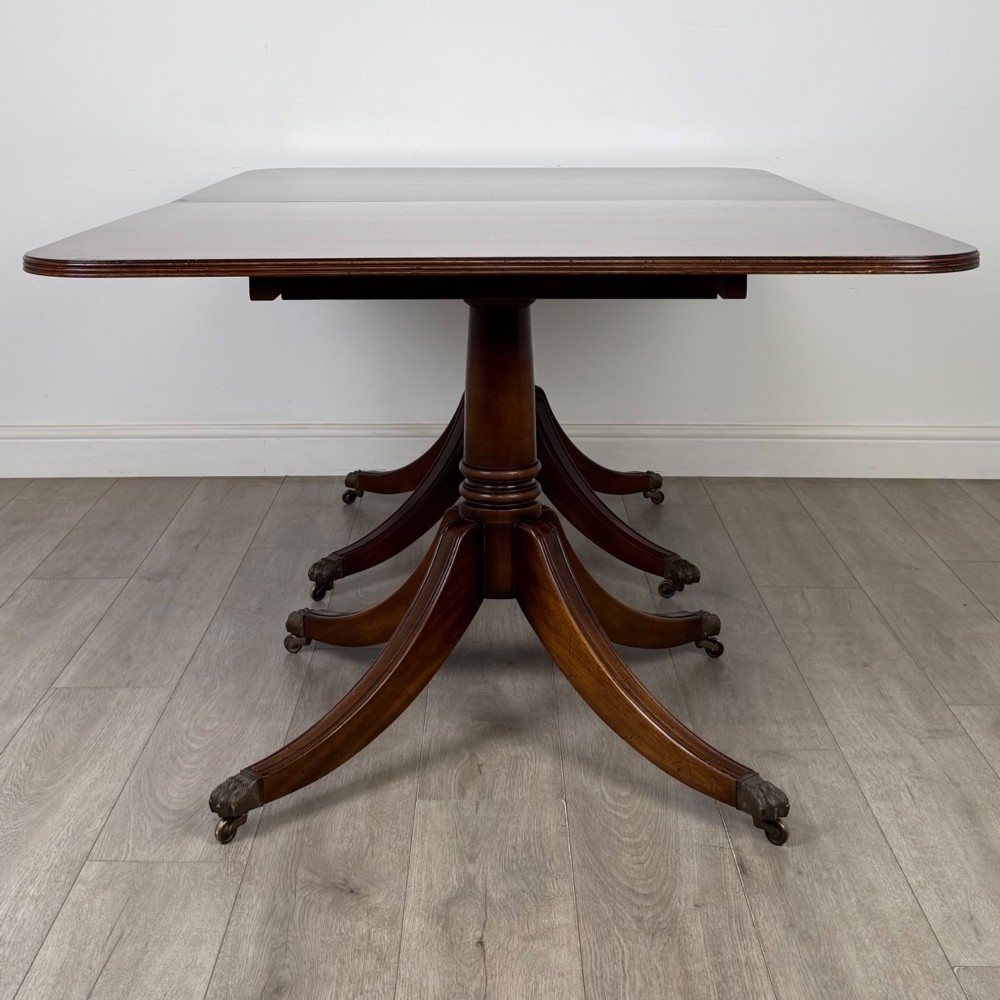 A 20th-century mahogany twin pedestal dining table featuring an extension leaf, reeded edges, and splayed quadruped feet with brass castors. View VI
