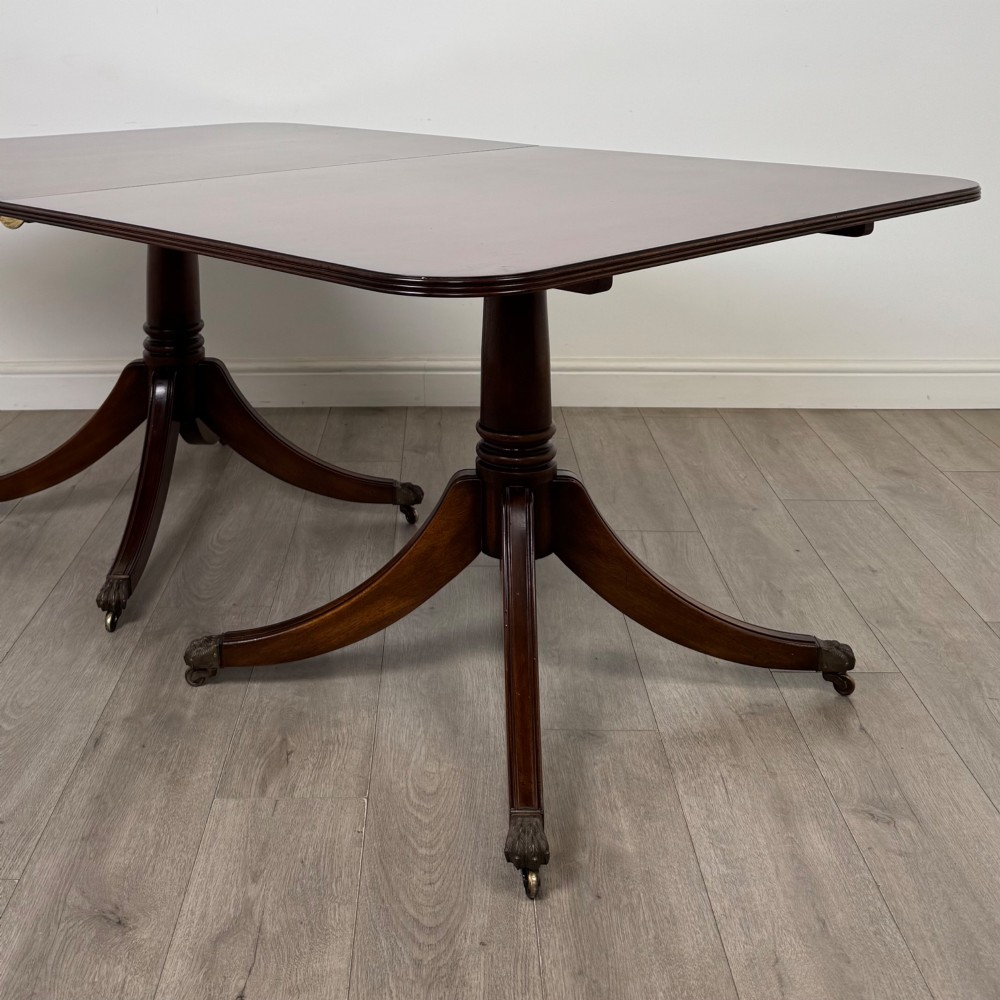 A 20th-century mahogany twin pedestal dining table featuring an extension leaf, reeded edges, and splayed quadruped feet with brass castors. View VII