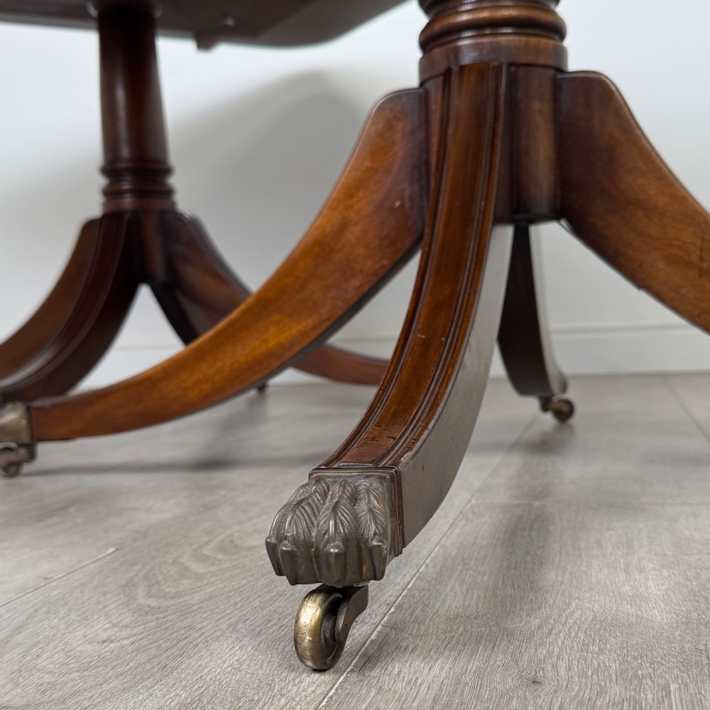 A 20th-century mahogany twin pedestal dining table featuring an extension leaf, reeded edges, and splayed quadruped feet with brass castors. View VIII