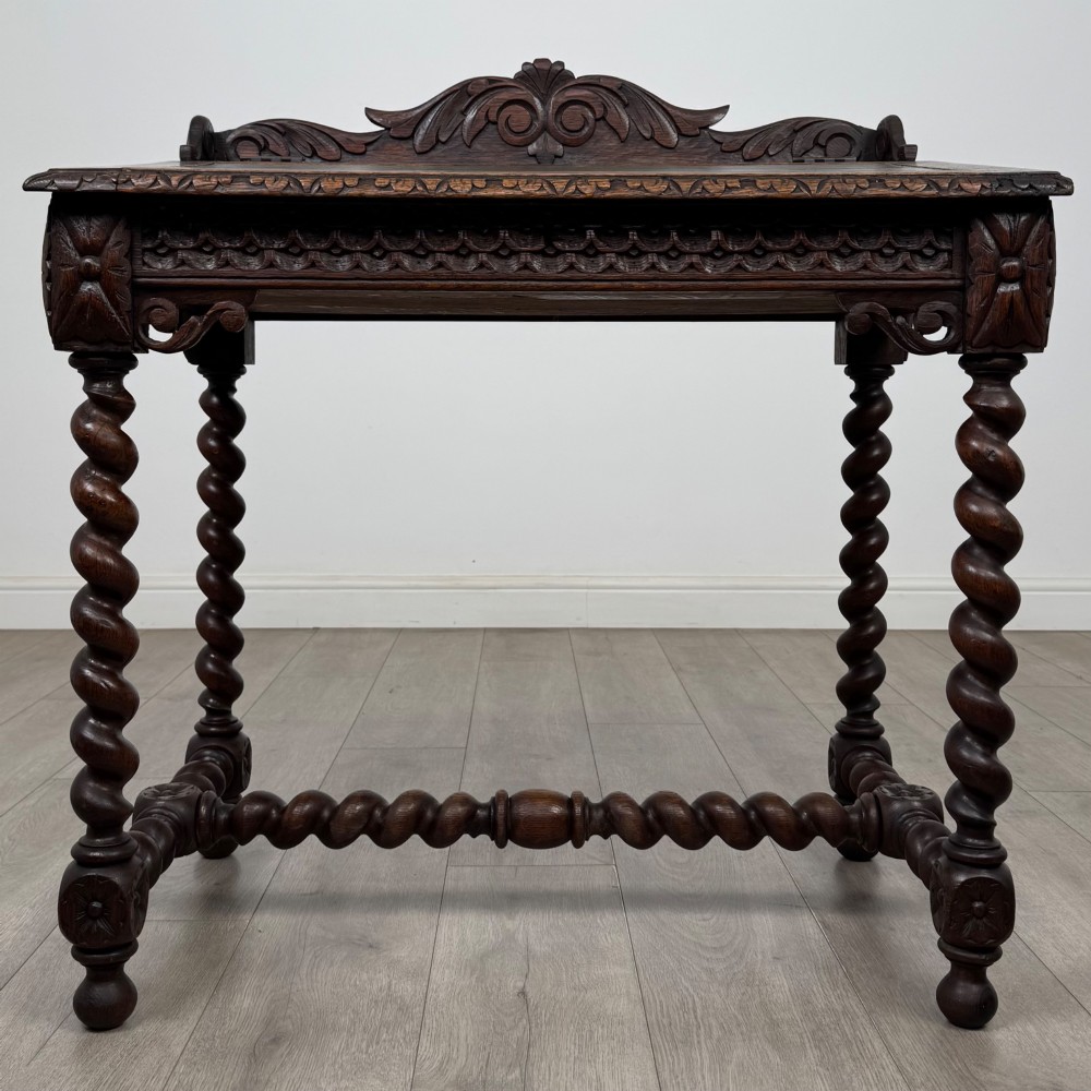 A 19th-century dark oak writing table featuring barley twist legs, carved stretchers, and an ornate carved cresting rail along the top gallery.