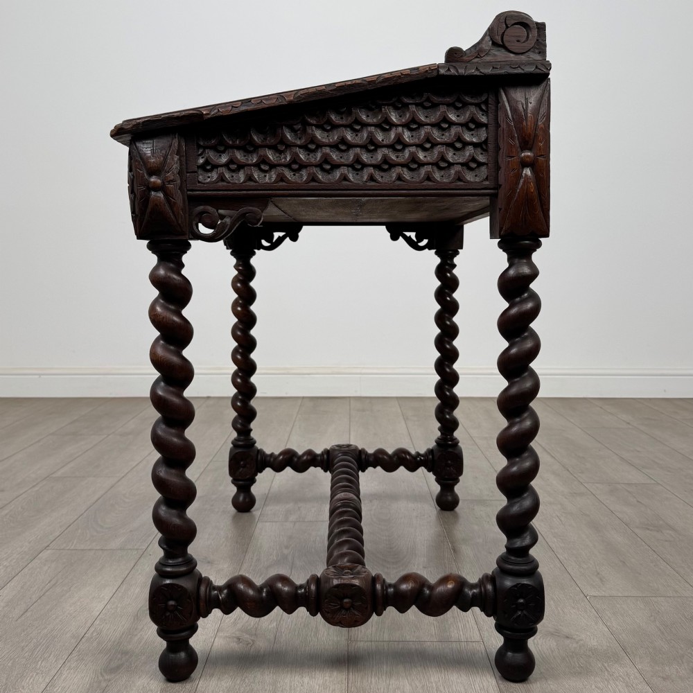 A 19th-century dark oak writing table featuring barley twist legs, carved stretchers, and an ornate carved cresting rail along the top gallery. View III