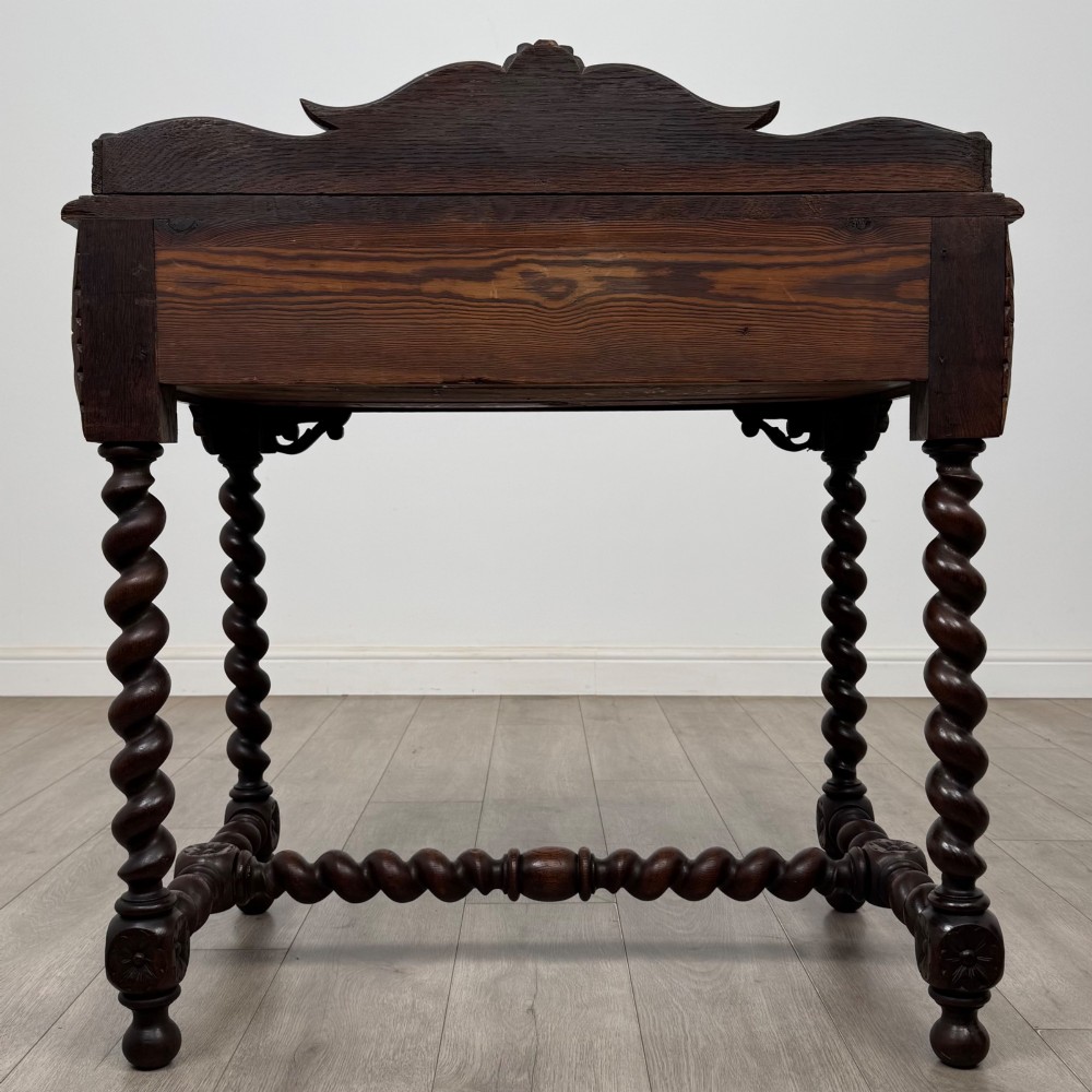 A 19th-century dark oak writing table featuring barley twist legs, carved stretchers, and an ornate carved cresting rail along the top gallery. View V