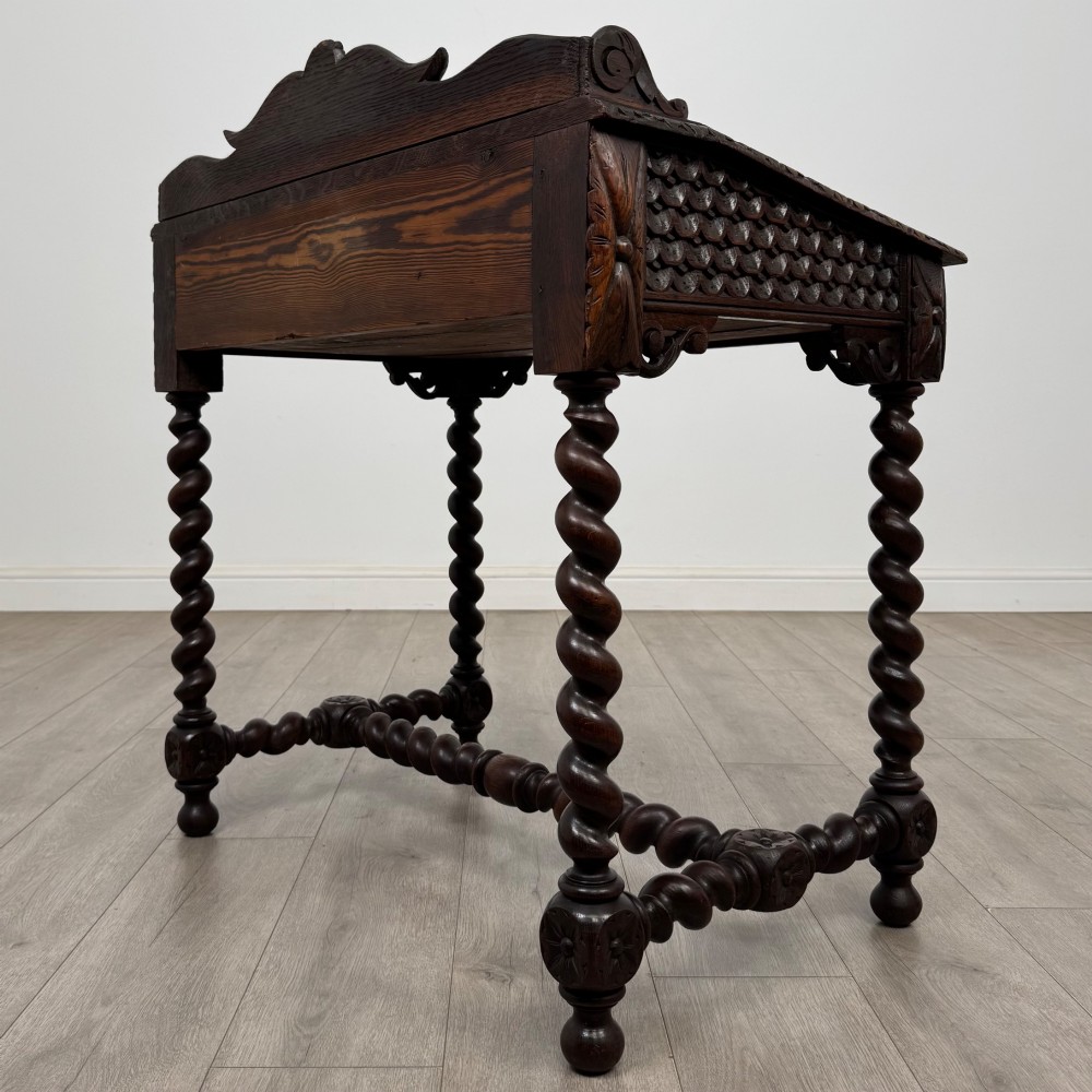 A 19th-century dark oak writing table featuring barley twist legs, carved stretchers, and an ornate carved cresting rail along the top gallery. View VI