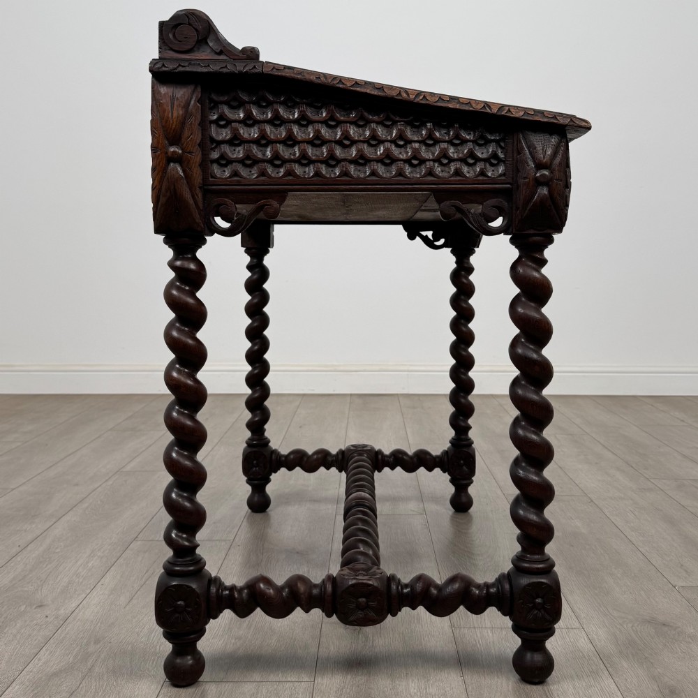 A 19th-century dark oak writing table featuring barley twist legs, carved stretchers, and an ornate carved cresting rail along the top gallery. View VII