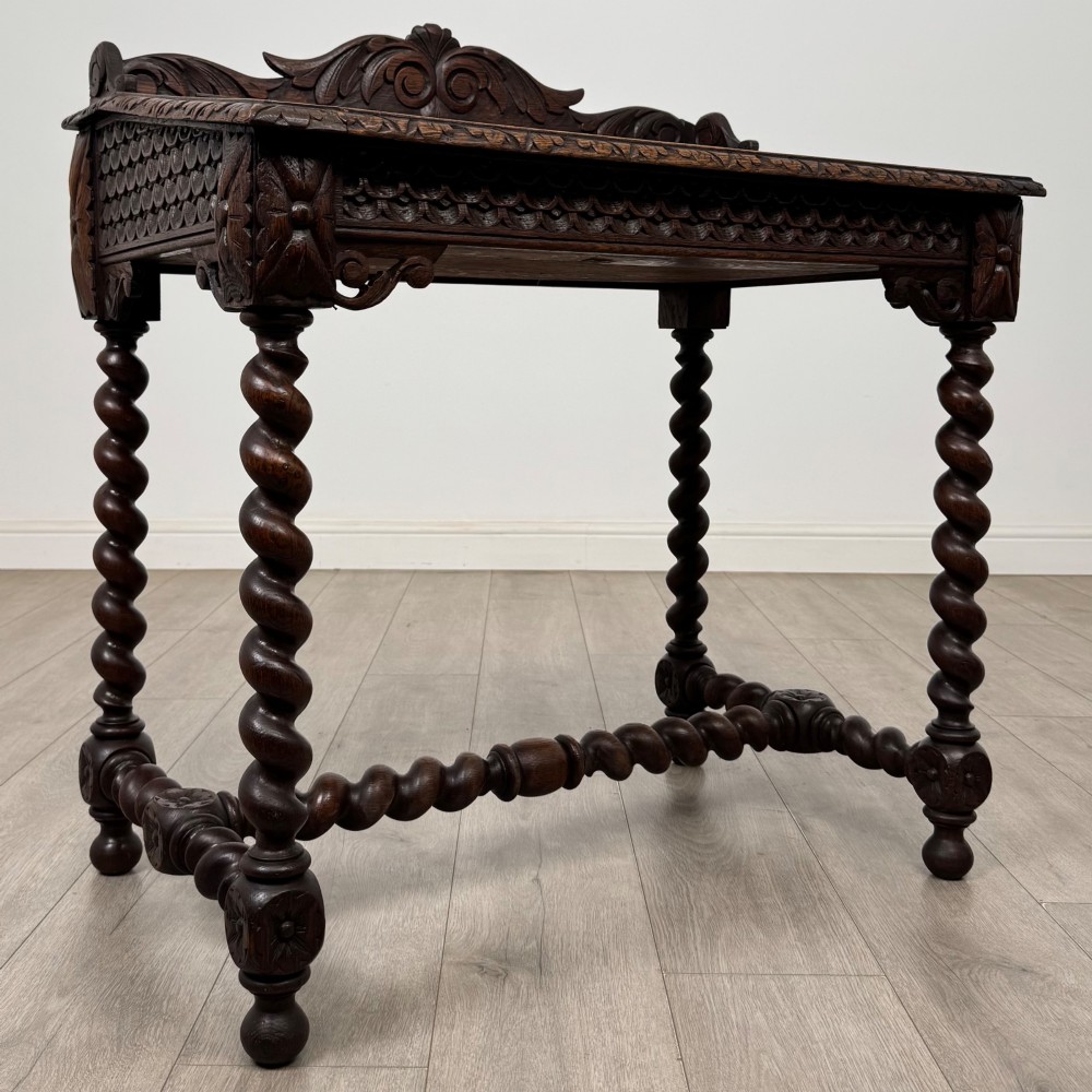 A 19th-century dark oak writing table featuring barley twist legs, carved stretchers, and an ornate carved cresting rail along the top gallery. View VIII